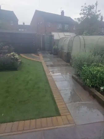 Back garden with colored indian sandstone patio pathway around half meter wide with new brick each side of the pathway.