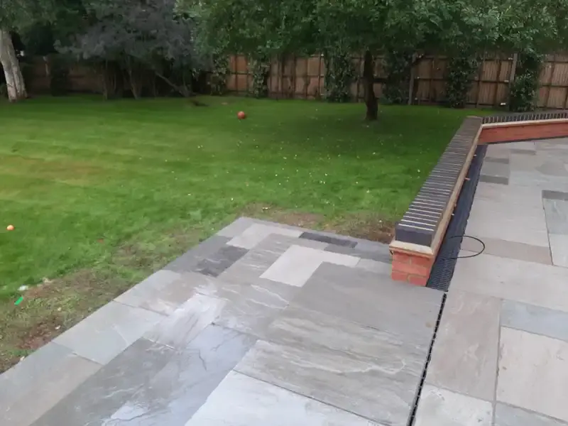 image of back garden grey indian sandstone patio, new red bricks with a black brick on top layer.