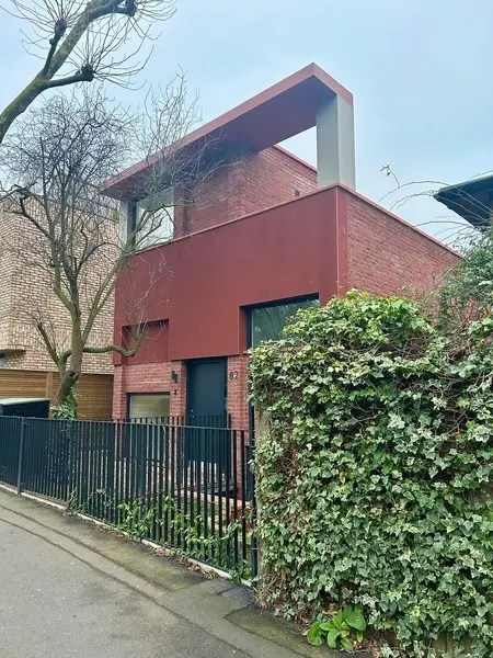 image taken from a side, of a new three story modern house build, bricks are in red.