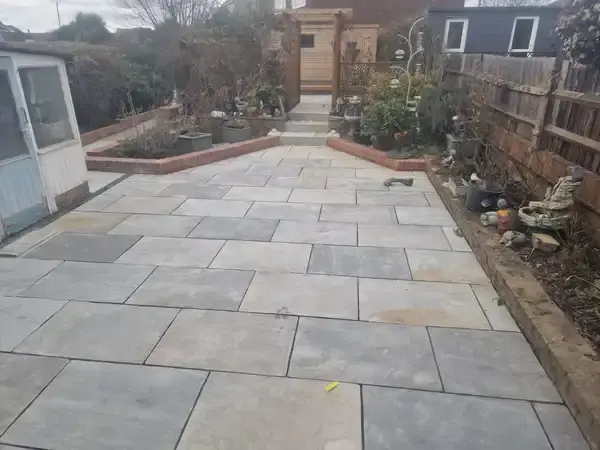 image of back garden , grey indian sandstone patio with a tiny wall of height two bricks around the edges of the patio.