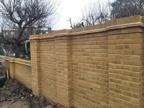 A new back Garden wall of yellow bricks about two meters high and around three meters long. 