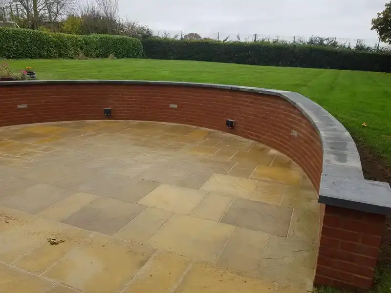 A new long Garden wall of red bricks half meter high in a curved circle of a radius 180 degrees. Top later of bricks, covered if a greyish colored tile.