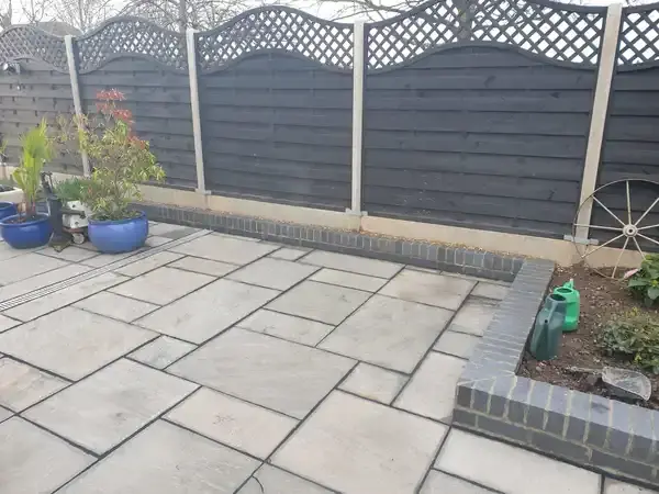 New back garden of grey indian sandstone patio and a small grey brick surrounding edge wall brickwork