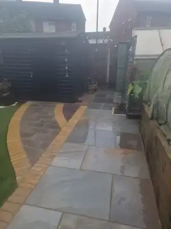Back garden with colored indian sandstone patio pathway around half meter wide with new brick each side of the pathway.