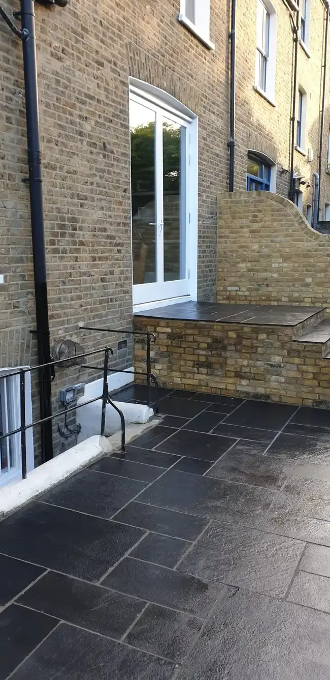 image of a new garden patio with black slabs and grey pointing. The steps brickwork matching exterior of the house with a black patio slabs on top of steps